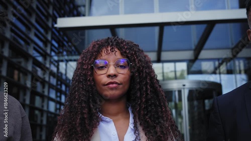 Panning shot reveals a diverse team as faces appear one by one, each holding a serious gaze toward looking at camera at a modern office entrance. Urban corporate mood, strong eye contact.