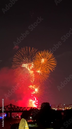 Vibrant fireworks show lights up night sky above city skyline, reflecting over river.Dazzling explosion of colors creates festive atmosphere 
