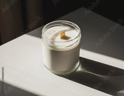 Minimalist Candle Jar Mockup with Blank Label and Wooden Wick, Illuminated by Dramatic Sunlight and Shadow.
