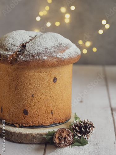 Vertical image of an isolated panettone, Christmas lights with bokeh effect in the background, on a white wooden table with free space for text