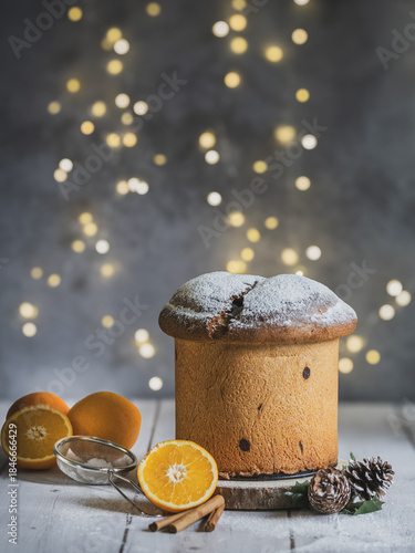 Traditional Italian handmade panettone on a wooden table with orange and cinnamon. Christmas lights with bokeh effect in the background. Copy space
