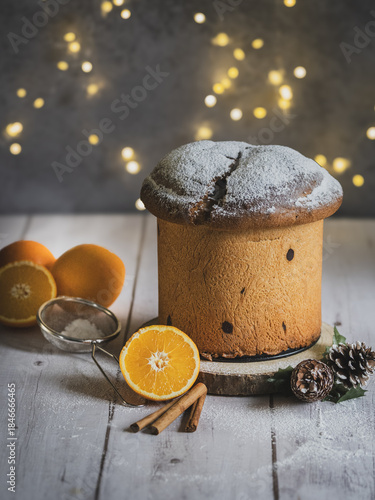Traditional Italian handmade panettone on a wooden table with orange and cinnamon. Christmas lights with bokeh effect in the background.