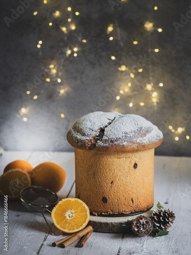 Traditional Italian handmade panettone on a wooden table with orange and cinnamon. Christmas lights with bokeh effect in the background.