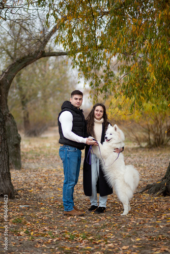 A young family - a guy, a girl and a cute fluffy Samoyed - are walking by the river