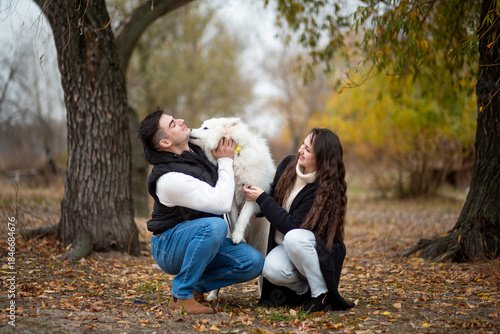 A young family - a guy, a girl and a cute fluffy Samoyed - are walking by the river