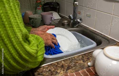 Older person washing dishes by hand in a sink, a common household chore in a typical kitchen setting