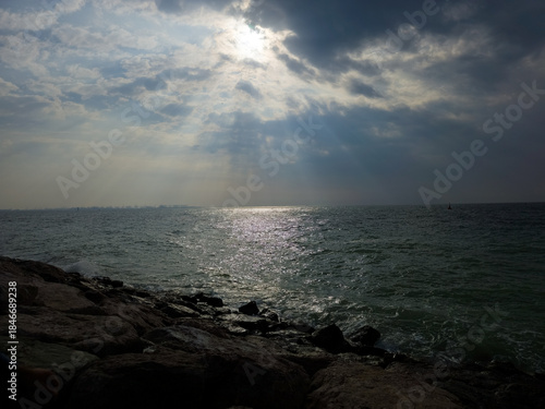 Sunset view from cloudy sky over the Sea with Rocks at beach. A beautiful sunset over the ocean with a large rock in the foreground. The sky is a mix of orange and pink hues, and the water is calm