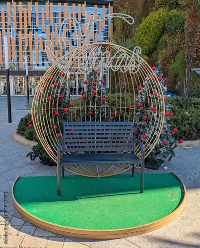 Banco de metal con árboles de navidad decorados con bolas de navidad y palabra Xmas en neón en el exterior de un centro comercial 