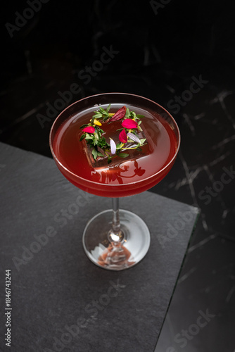 An elegant cocktail with a vibrant red hue, garnished with edible flowers and herbs, resting on a sophisticated surface. The drink exudes an aura of luxury and refinement. 