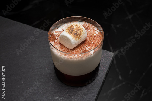 An overhead shot of a delicious marshmallow cocktail. A clear glass is placed on a stone surface 