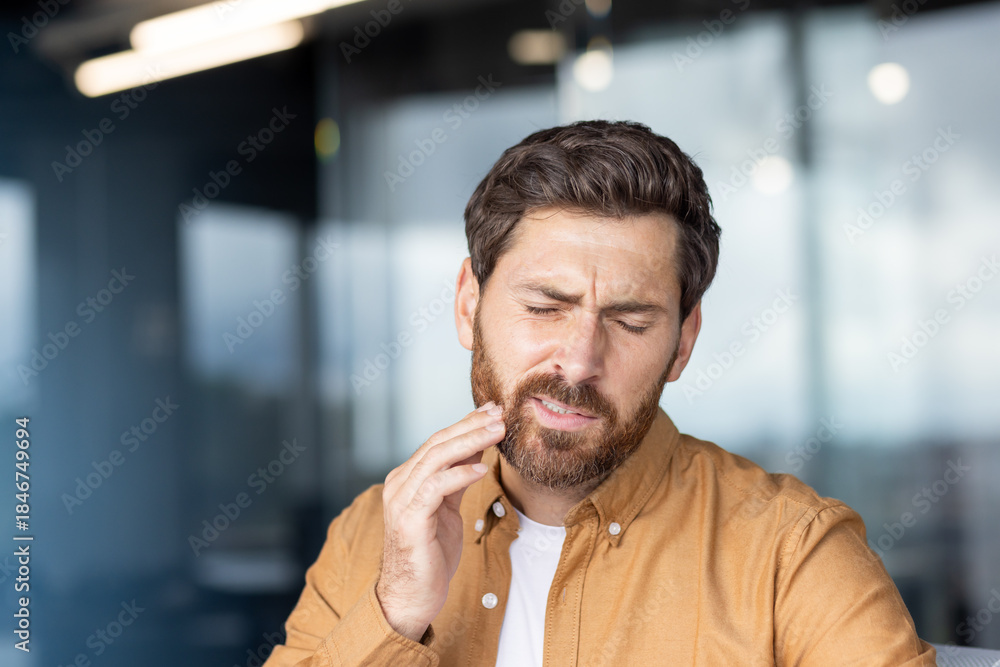 Obraz premium Young man experiencing an acute toothache or dental pain, touching his jaw with a hand, depicting discomfort, dental problems, and the need for urgent dental care or treatment