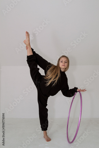 A young rhythmic gymnast in a black tracksuit performs elements with a hoop