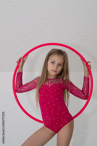 A young rhythmic gymnast in a bright pink leotard is training with a hoop