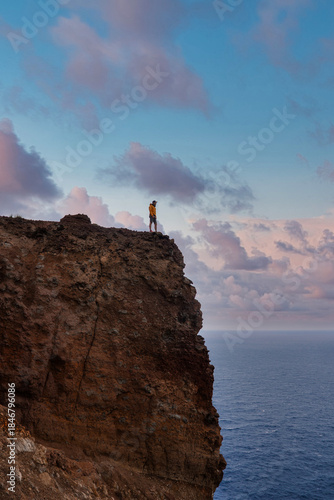 Wallpaper Mural A hiker in a yellow jacket stands on Ponta de Sao Lourenco, Madeira, Portugal, facing the Atlantic as pastel clouds drift. Vertical composition with soft evening light. Torontodigital.ca