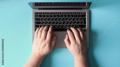 Hands typing on a laptop keyboard against a blue background. Flatlay concept, advertising remote work