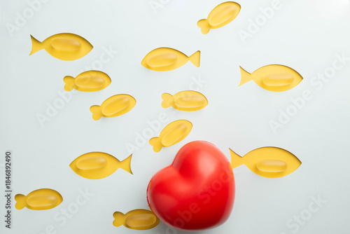 Fish oil soft gel capsules, dietary supplements containing Omega 3 for heart health.  Yellow fish with blue background with a big red heart.  Heart health month February.