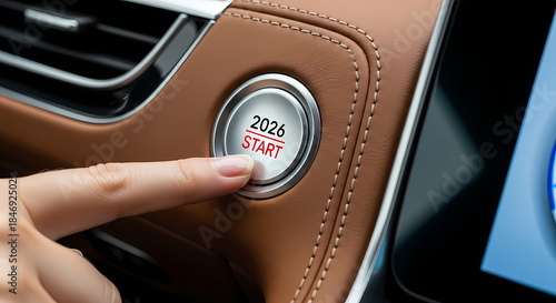 Closeup of finger pressing car ignition button with 2026 start label on silver and brown interior