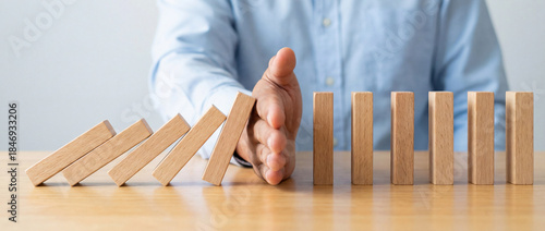 Businessman stopping domino effect on wooden table