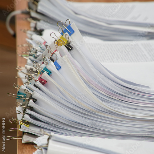 Huge stacks of sorted paper documents with colorful binder clips on a wooden office desk. Concept of bureaucracy and heavy administrative workload. Photo