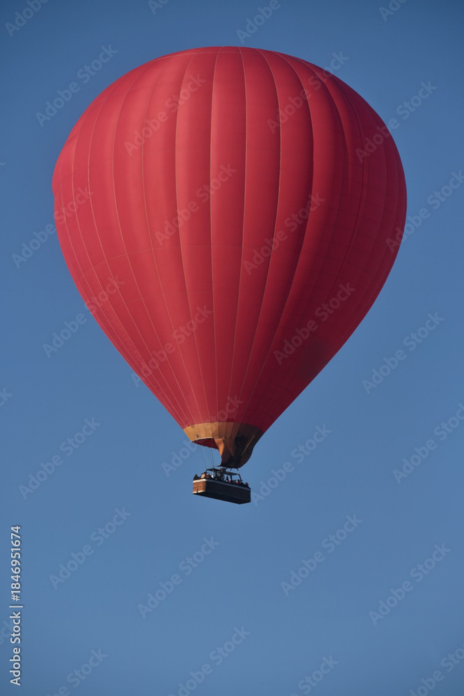Obraz premium A red hot air balloon floating high in a clear blue sky, captured from below, with smooth fabric panels and a small basket hanging beneath.