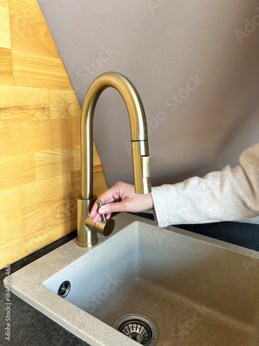 Фотография Woman hand turning on kitchen faucet with running water at sink, everyday househ