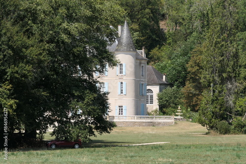 A view through lush green trees toward the tower of a French château.