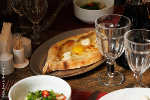 Traditional Georgian table with Adjarian Khachapuri, fresh salads, drinks and glassware