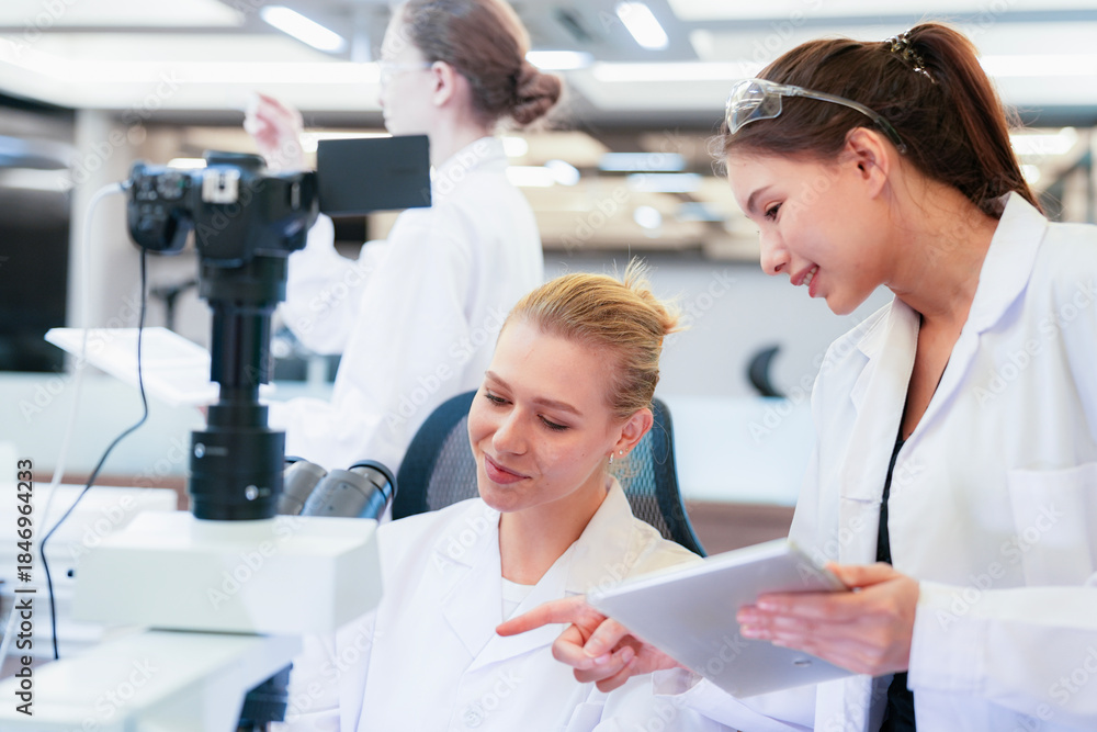 Fototapeta premium Diverse team of female scientists working in busy digital pathology lab. Researchers analyzing histology slides using microscope, tablet, and visual inspection for medical diagnosis.