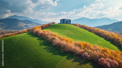 A modern building sits on top of a green hill surrounded by colorful autumn trees