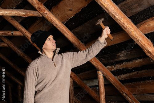 A male roofer hammering nail into wooden frame of roof construction