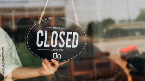 Closed sign hanging on glass door of small business shop. Concept of store closed, after hours service, retail schedule, business hours notice, customer communication and storefront signage.