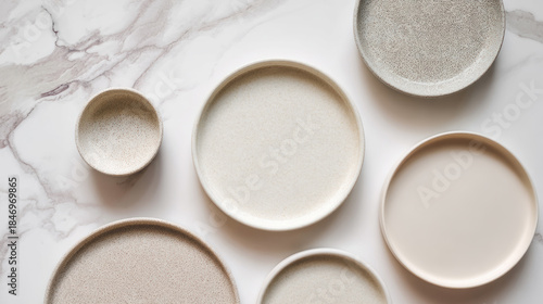 Minimalist speckled ceramic plates and bowl arranged on marble kitchen countertop in daylight