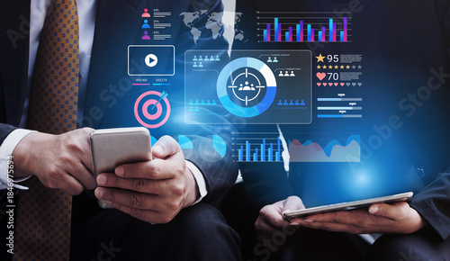 Wallpaper Mural Two business professionals engage with mobile devices while analyzing digital data, showcasing a modern workspace with graphs and statistics that highlight teamwork and technology. Gantry Torontodigital.ca