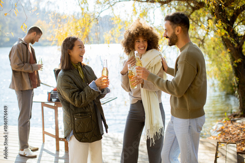 Friends celebrate by the lakeside, enjoying drinks and playfulness on a sunny day