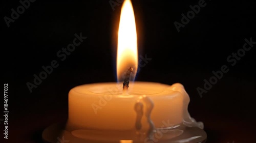 Close-up of a hand lighting a white candle with a wooden match stick in a dark room casting a warm glowing light on the melting wax and flame.