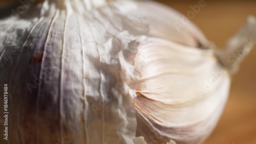 Close Up Detailed Macro Shot Of A Whole Garlic Bulb With Papery White Skin And Subtle Purple Hues On A Warm Wooden Surface Illuminated By Soft Natural Light
