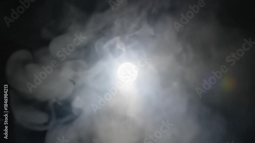 Bright Orb of Light Partially Obscured by Wisps of White Smoke Against a Dark Background with Subtle Lens Flare Effect