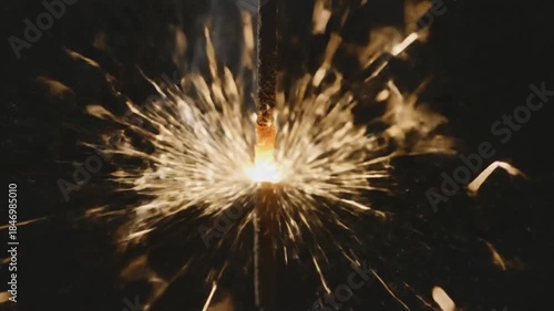 Close up of a bright sparkler glowing with intense golden sparks against a dark black background during a celebration event capturing the festive atmosphere and celebratory light effects