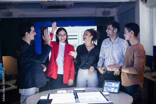 Foto Diverse group of professionals celebrating successful teamwork high-fiving and smiling enthusiastically around a table with tablets displaying app designs