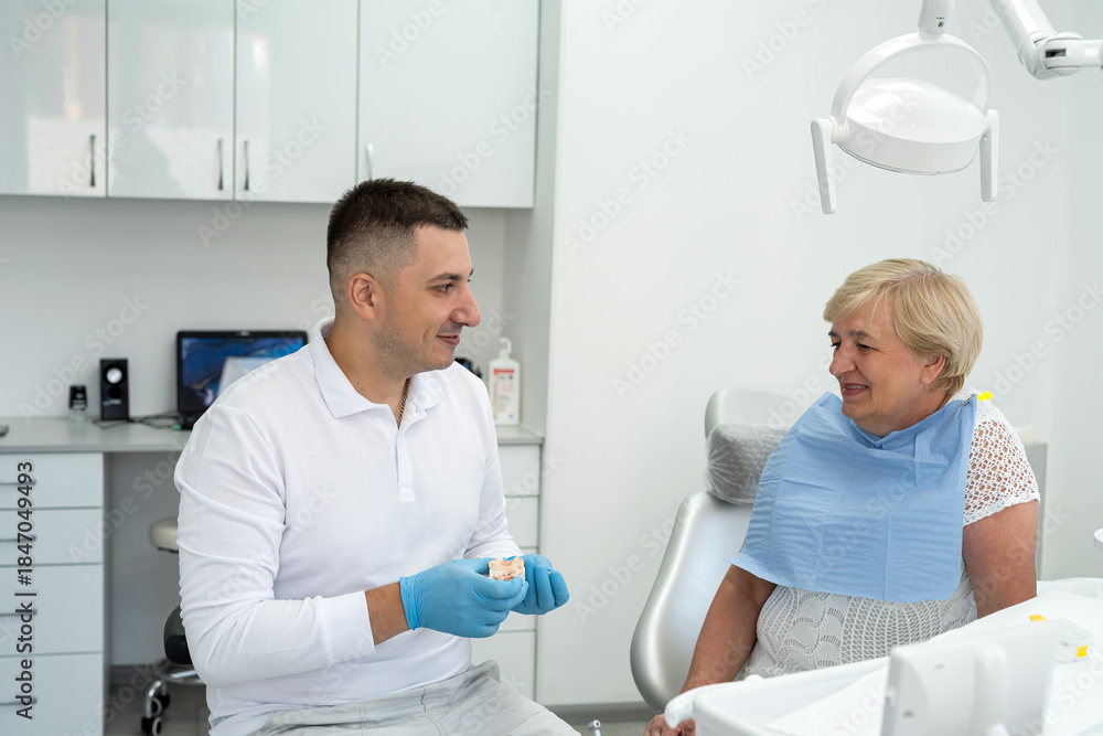 Fototapeta premium dentist consulting a retired woman with the installation of a tooth crown, an implant. Artificial teeth with steel pin
