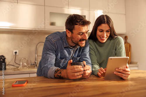 Bild auf Leinwand Couple using tablet computer and drinking coffee in the kitchen at home