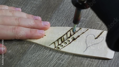A child hand draws circle ornaments by wood burning, pyrographic on a wooden kitchen turning plate