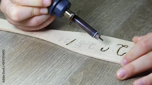 A childs hand writes by burning wood, pyrographic New Years text 2025/26