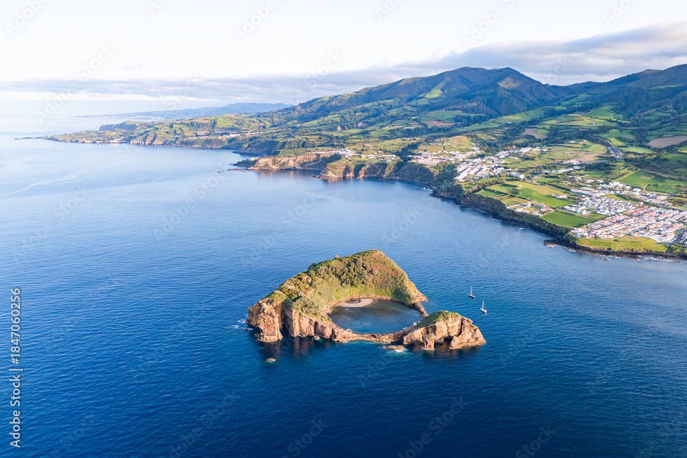 Obraz premium Volcanic islet lagoon with shallow sandy area and rock walls near Azorean coastline, drone view