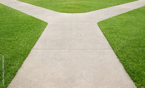 Symmetric concrete path splitting into two directions through a vibrant green lawn