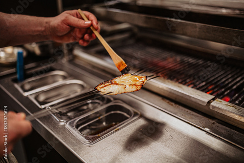 Close-up shot of a professional chef's hands skillfully preparing a grilled sea bass in a restaurant kitchen