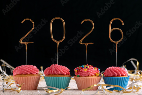Holiday cupcake with pink glaze and 2026 numbers on black background. New Year and Christmas.