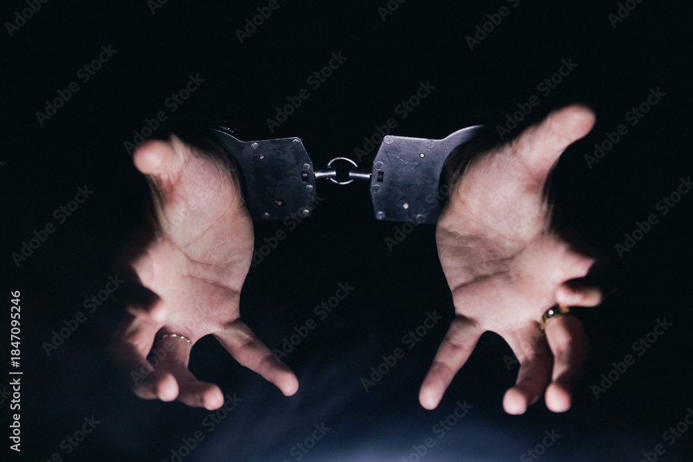 Obraz premium Hands in handcuffs are raised against a dark background, symbolizing restraint and captivity, evoking themes of justice, freedom, and the struggle against oppression