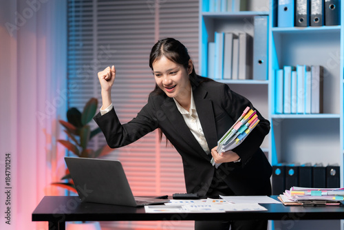 Quadro em tela Businesswoman celebrates success at her desk: An enthusiastic businesswoman, radiating with triumph, pumps her fist in the air