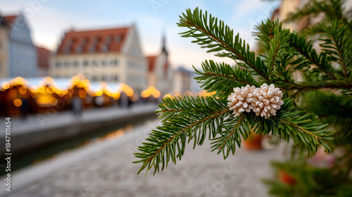 Fototapeta Naklejka Na Ścianę i Meble -  Pine branch by market stalls. A pine branch with white decorations is in the foreground with market stalls lit up in the background during evening.